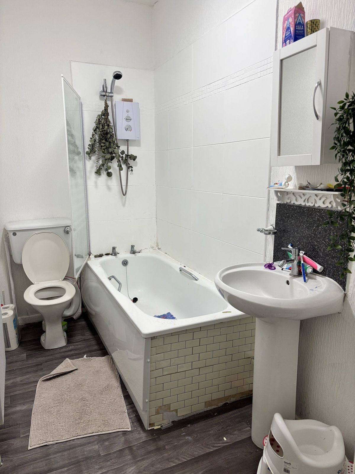 Bathroom before: dated tiles, electric shower and pedestal sink