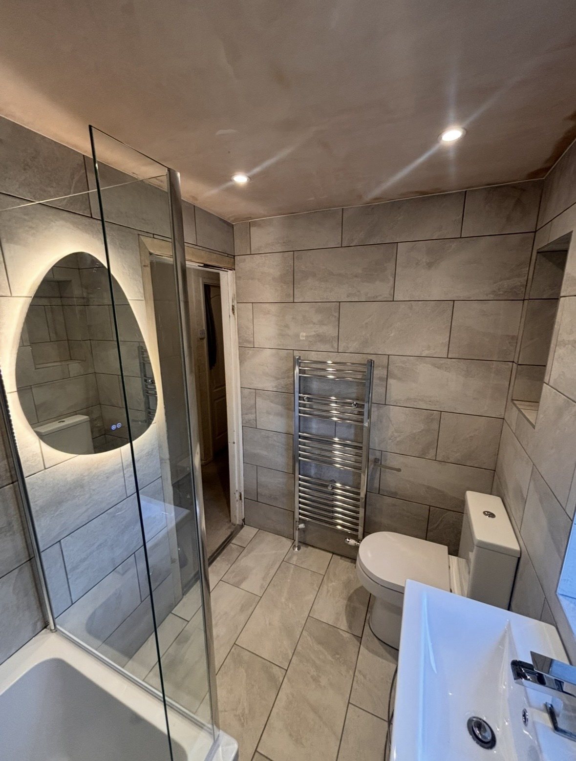 After: one seamless modern bathroom with grey tiles and backlit mirror
