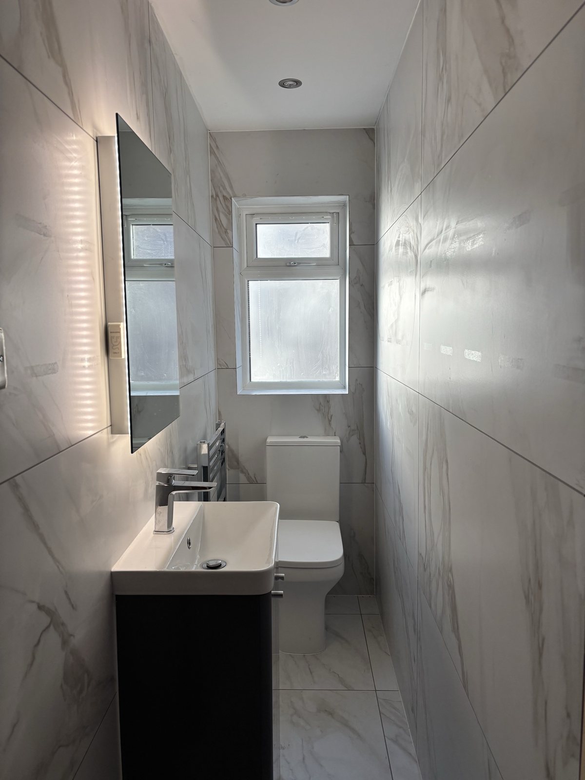 Finished modern W/C with marble-effect tiles and LED mirror, after